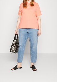 Ljus korallfärgad pikétröja med knappkrage, blå högmidjade jeans, svarta platta sandaler och en svartvitt vävd handväska.