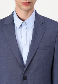 Jūras spēku piedurknis žakete ar vienu pogu, apvienota ar gaiši zilas krāsas krekla ar norādītu apkakli.