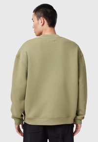 Sudadera verde oliva con un ajuste holgado, cuello redondo, hombros caídos y puños acanalados, hecha de una tela texturizada suave.