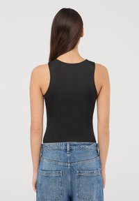 Czarny bezrękawnik z gładką fakturą, dopasowanym krojem i wysokim dekoltem, zestawiony z niebieskimi szortami dżinsowymi z wysokim stanem.