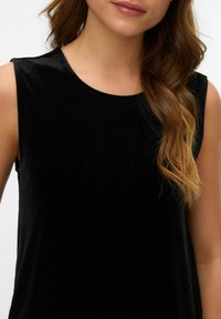 Svart ärmlös topp i mjukt, plyschigt tyg med rund halsringning och slät yta. Enkelt mönster utan synlig hårdvara eller tryck.