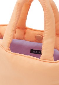 Persikofärgad tote-väska med kviltad textur, två handtag och lila foder. Har en synlig varumärkesetikett inuti.