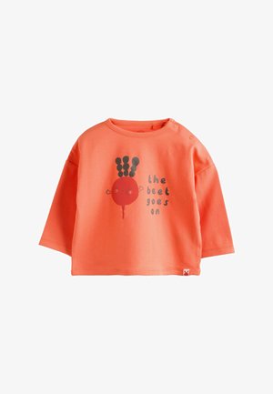 Chemise corail à manches longues en coton, ornée d'un graphique de betterave rouge avec des feuilles noires et le texte "the beet goes on". Fermeture à pression à l'épaule.