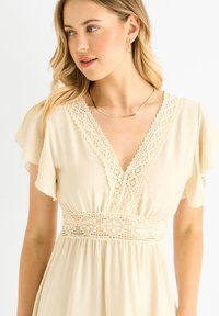 Beige dress with lace trim along the V-neck, short flutter sleeves, and a crochet waistband. Soft fabric with a flowy design.