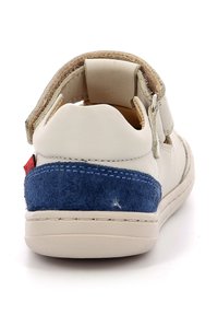 Zapato de piel blanca con acento de ante azul en el talón, correa ajustable y interior acolchado. Presenta un detalle de costura alrededor de la suela.