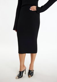 Zwarte geribbelde breimidirok met een aansluitende Silhouette. Gecombineerd met zwarte muiltjes met een spitse neus en metalen gouden accenten.