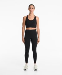 Svart sport-bh med rundad halsringning och figurnära passform, i kombination med högmidjade svarta leggings och ljusa träningsskor.