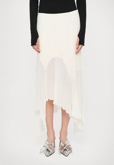 White asymmetric skirt with sheer layers, flowing texture, and a raw hem, paired with silver pointed-toe slip-on shoes.
