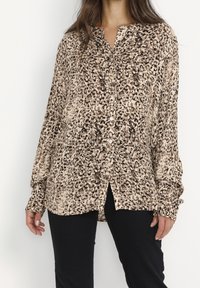 Leopard print button-up shirt in beige and brown tones, featuring a collar, long sleeves, and a relaxed fit with side splits.