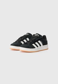 Black suede sneakers with white three-stripe design, flat laces, cushioned tongue, and a rubber sole in a contrasting beige color.