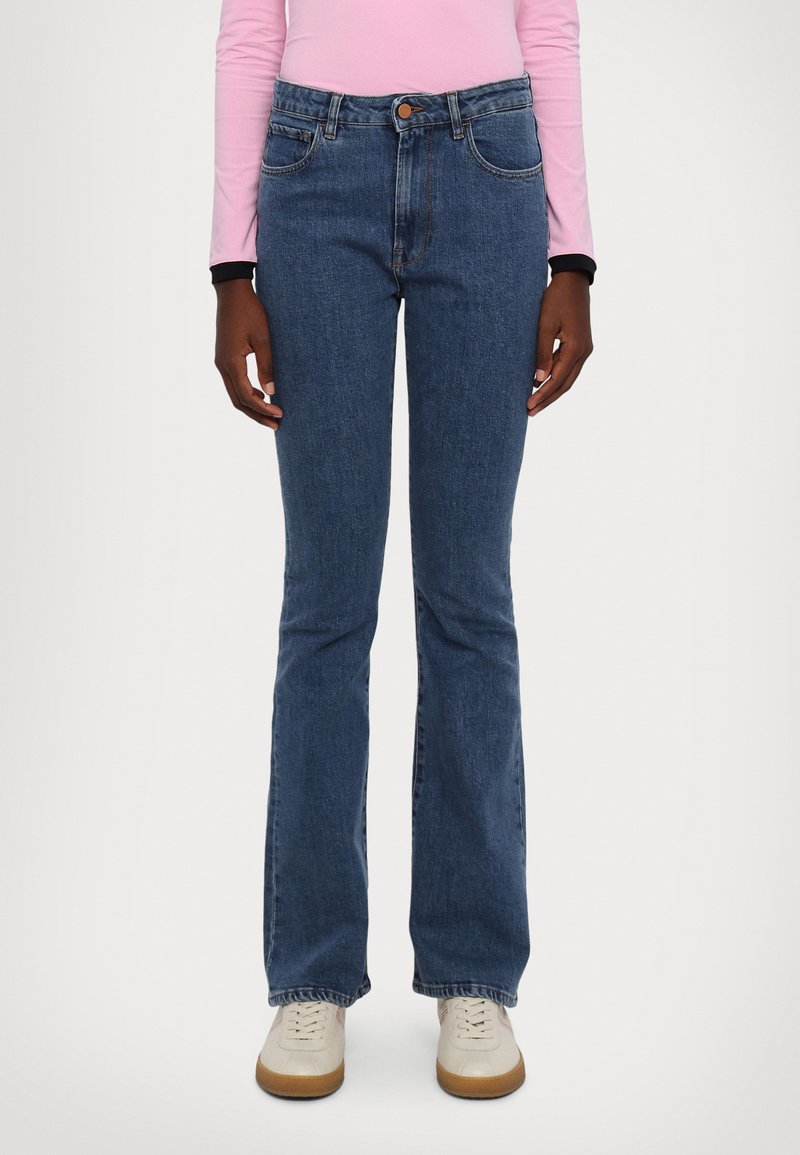 Blue denim flared jeans with a high waist, two front pockets, and a central button. Paired with light-colored sneakers.