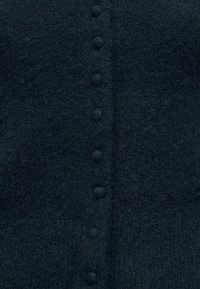 Κοντινή λήψη σκούρου υφασμάτινου υφάσματος με μια κάθετη σειρά μικρών κουμπιών καλυμμένων με ύφασμα ραμμένων στο κέντρο.