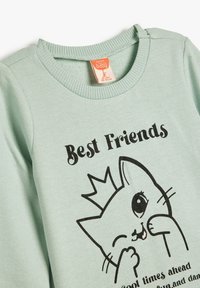 Mintgroene katoenen sweatshirt met een speelse kat graphic, zwarte tekst leest "Beste Vrienden," met ribgebreide halslijn en boorden.