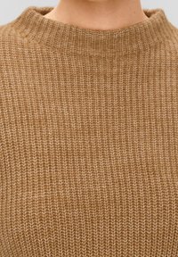 Brązowy sweter z dzianiny o prążkowanej fakturze i wysokim kołnierzu, eksponujący gęsty wzór splotu i ciepły, neutralny kolor.