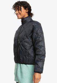 Black puffer jacket with a diamond quilted pattern, high collar, and full front zipper. Made of shiny, smooth fabric with a relaxed fit.