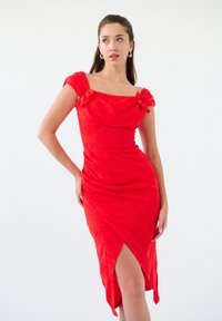Robe rouge ajustée avec un décolleté carré et de courtes manches froncées. Le tissu présente un motif floral subtil et une fente latérale pour plus de liberté de mouvement.