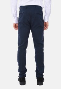 Pantaloni chino blu navy realizzati in misto cotone, con vestibilità slim, due tasche posteriori con zip e una texture liscia. Si coordinano con una camicia bianca.