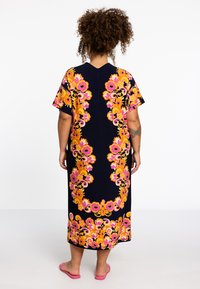 Blumiges Maxikleid in Marineblau mit lebendigen pinken und gelben Mustern, kurzen Ärmeln, V-Ausschnitt und einem lässigen Schnitt. Getragen mit pinken Sandalen.