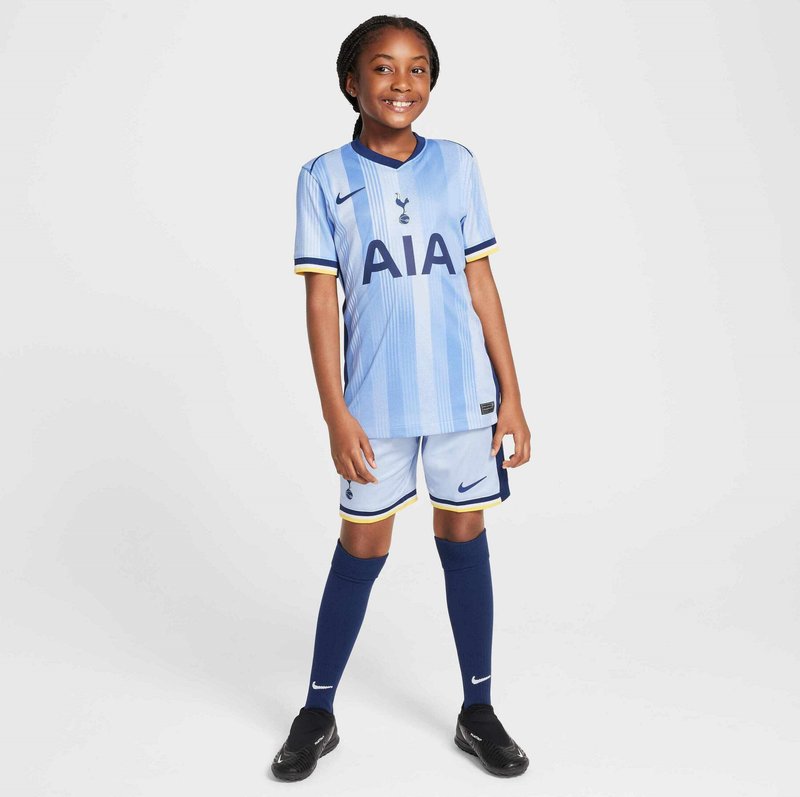 Helles blaues Fußballtrikot mit vertikalen Streifen, schwarzem "AIA"-Logo, marineblauen Akzenten und passenden Shorts. Schwarze Stollenschuhe und knielange marineblaue Socken.