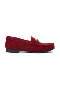 Mocassin en daim rouge avec semelle noire et détail mors doré sur le dessus, profil latéral visible sur fond blanc.