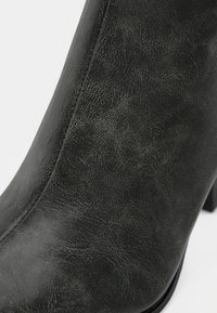 Black synthetic ankle boot with a textured finish, slightly curved shape, and a block heel. Features subtle stitching details.