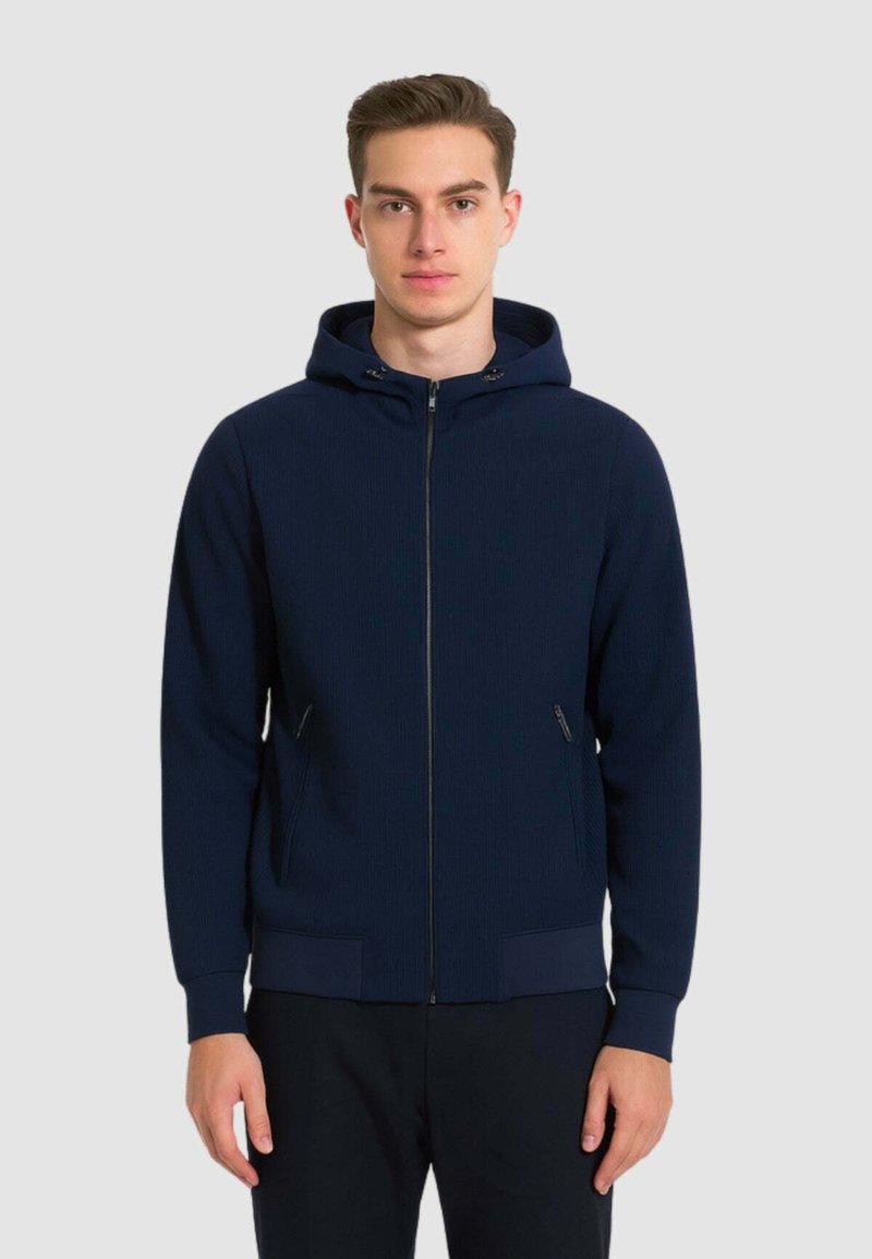 Felpa con zip navy in tessuto a costine, con cappuccio regolabile, chiusura frontale con zip e tasche laterali con accenti eleganti.