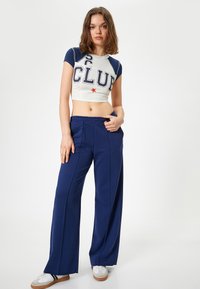 Top corto de manga corta en blanco con acentos en azul marino y letras grandes, combinado con pantalones anchos azul marino y zapatillas blancas.
