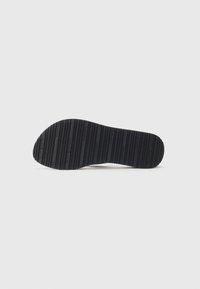 Semelle de chaussure noire avec des rainures horizontales et le logo "Tommy Hilfiger" répété sur un fond blanc uni.