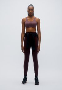 Αθλητική εμφάνιση με μπορντό αθλητικό μπουστάκι και ταιριαστό κολάν. Μαύρη φούτερ ζακέτα δεμένη στη μέση, σε συνδυασμό με μαύρα αθλητικά παπούτσια.