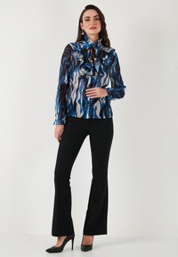 Bluish patterned blouse with ruffles and a tie neck, paired with black flared pants and heels. Smooth texture with a flowy design.