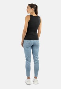 Schwarzes ärmelloses Oberteil, kombiniert mit hellblauen Jeans. Das Oberteil hat eine glatte Textur, und die Jeans verfügen über Gesäßtaschen und eine figurbetonte Passform.
