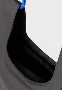 Μαύρη υφασμάτινη τσάντα ώμου με λεία υφή, που διαθέτει μπλε χερούλι και εσωτερική τσέπη με φερμουάρ. Μινιμαλιστικός σχεδιασμός και λειτουργικό σχήμα.