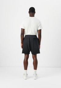 Črne kratke hlače s sproščenim krojem, ki imajo dva stranska žepa, neobdelan rob in elastičen pas. V kombinaciji z belim majico in belimi čevlji.