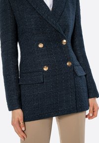 Marineblauer strukturierter Blazer mit doppelt geknöpfter Vorderseite und goldenen Knöpfen. Verfügt über zwei vordere Taschen und strukturierte Revers.