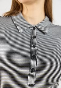 Sort-hvid stribet polo skjorte med krave, udstyret med seks sorte knapper og en blød stoftekstur.