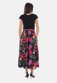 Donna che indossa una maglietta nera a maniche corte e pantaloni a vita alta e gamba larga con motivi floreali rosa, rossi e verdi, vista da dietro.