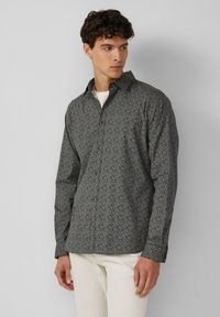 Lange mouwen overhemd met knopen in donkerblauwe stof met een wit bloemenpatroon. Voorzien van een gespreide kraag en een regular fit. In combinatie met lichtgekleurde broek.