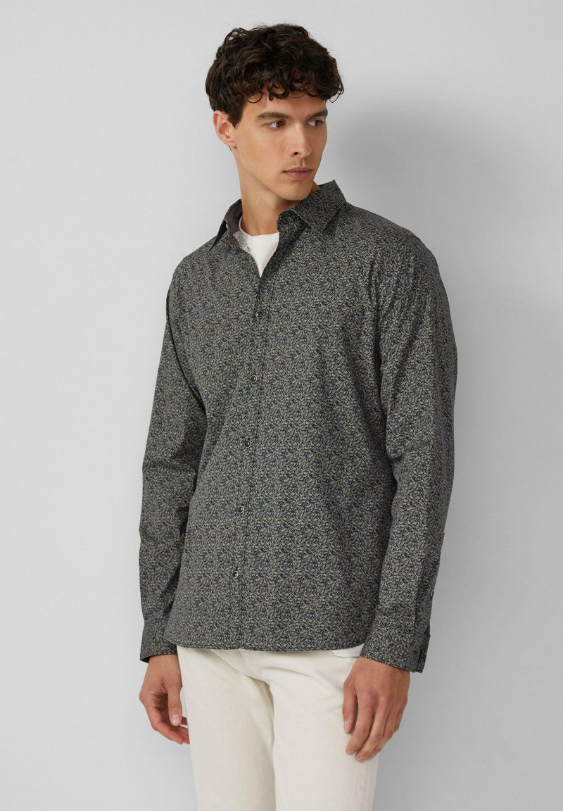 Lange mouwen overhemd met knopen in donkerblauwe stof met een wit bloemenpatroon. Voorzien van een gespreide kraag en een regular fit. In combinatie met lichtgekleurde broek.