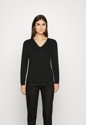 Maglione nero a maniche lunghe con scollo a V in tessuto morbido, caratterizzato da un design aderente e orlo a coste. Abbinato a pantaloni scuri.