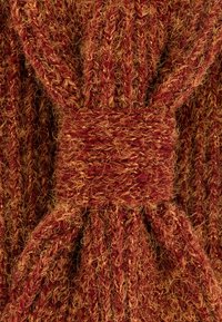 Gebreide stof in warme tinten van rood en oranje, met een gestructureerd patroon en een opvallende gedraaide knoopdetail in het midden.