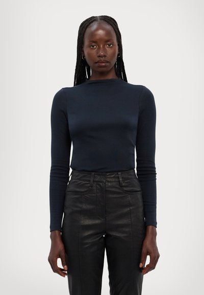 Marineblå langærmet top med en tætsiddende design og ribbet tekstur, parret med højtaljede sorte læderbukser med en glat overflade.