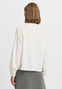 Leichte weiße Bluse mit langen, gepufften Ärmeln und strukturiertem Schulterdetail. Verfügt über einen runden Halsausschnitt und einen verkürzten Saum.