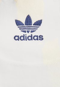 Vitt tyg med en broderad blå Adidas-logga med en trefotsdesign ovanför ordet "adidas", som framhäver rena linjer och textur.
