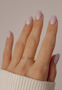 Anello d'oro con piccole pietre trasparenti, indossato su una mano con unghie di un leggero colore viola. Mano parzialmente coperta da un maglione lavorato a maglia di colore chiaro.