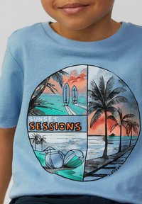 Jasnoniebieska koszulka z okrągłą grafiką przedstawiającą plażowe sceny, palmy, deski surfingowe oraz napis "ZACHODY SŁOŃCA SESJE" w pomarańczowym kolorze.