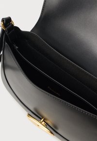 Crna kožna torba s glatkom teksturom, koja ima zlatni okrugli metalni detalj i mekani, neobloženi unutrašnjost.