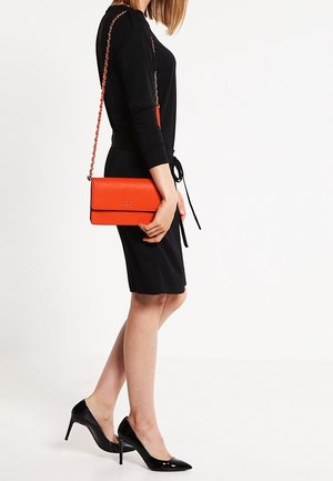 Oranžová texturovaná crossbody taška s řetízkovým popruhem, obdélníkového tvaru a klopou. Nosená s černými šaty a černými podpatky.