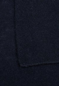 Marineblåt strikket stof med en blød tekstur, fremtrædende sømme og et lidt lysere rektangulært felt indimellem.