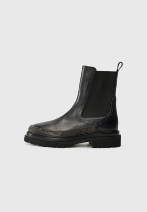 Bottine Chelsea en cuir noir avec panneaux élastiques sur les côtés, bout texturé et semelle en caoutchouc robuste, avec une poignée à l'arrière.