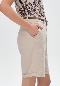 Beżowe szorty dopasowane z gładką fakturą, bocznymi kieszeniami i podwiniętymi mankietami; zestawione z wzorzystą górą w neutralnych odcieniach.